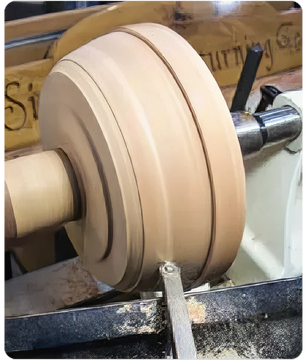 Close-up view of a wooden bowl being shaped on a lathe with a turning tool in a woodworking workshop setting.