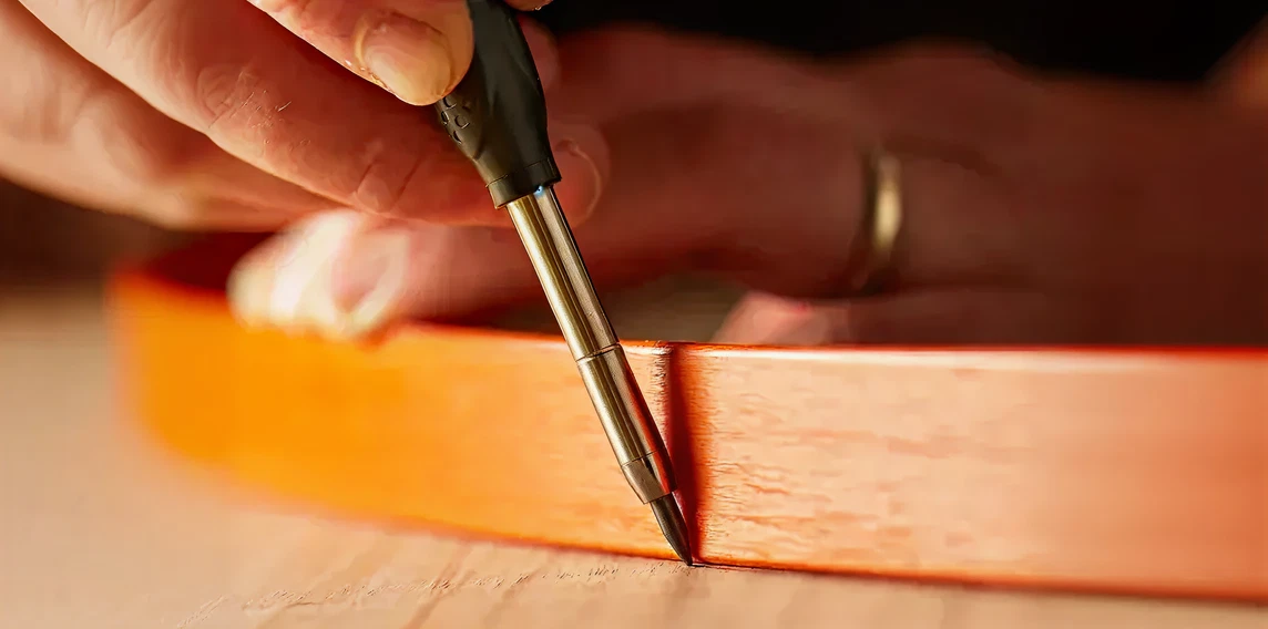 Close-up of a hand holding a mechanical pencil tracing carefully along the edge of a wooden surface, focused on precision work.